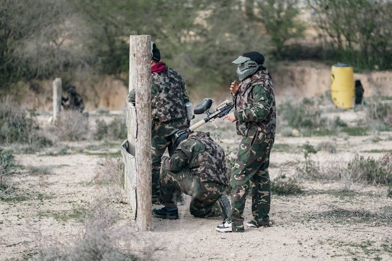 Group of adults in camouflage gear playing paintball outdoors for recreation.