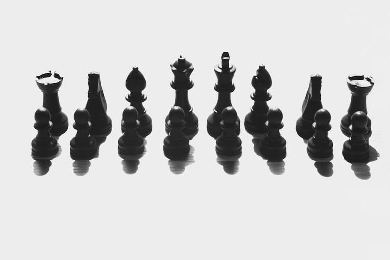 Black chess pieces arranged in a dramatic shadow cast on a white background.
