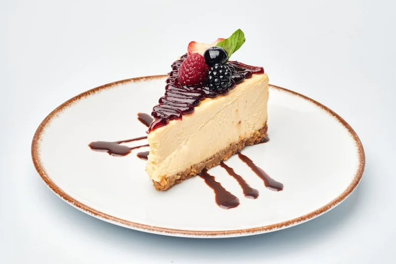 Rebanada de pastel de queso con frutos rojos frescos y un chorrito de coulis de frutas