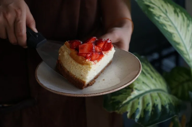 Manos de un chef cortando suavemente un pastel de queso perfecto, mostrando su interior liso