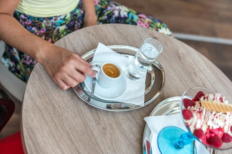 Café y postres variados dispuestos en una mesa, con una mano alcanzando una taza de café