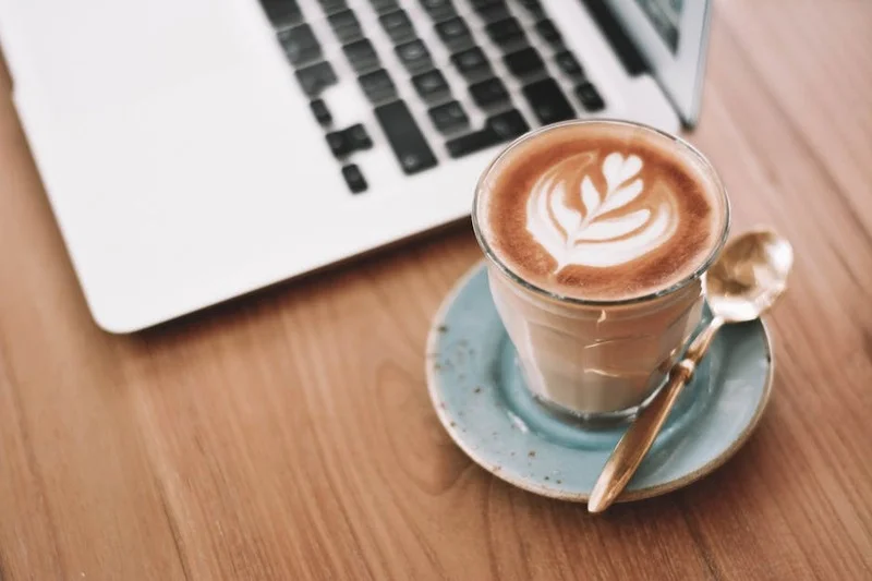 Latte de café con arte de espuma en mesa de madera junto a una laptop