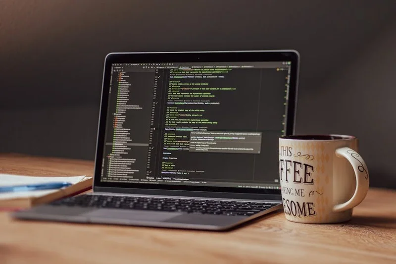 Vista aérea de laptop de desarrollador con código en pantalla, filtro de privacidad y taza de café