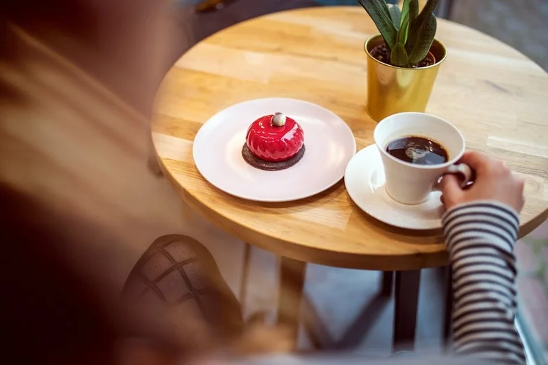 Una persona disfrutando de una taza de café con un pequeño postre en un acogedor ambiente de cafetería